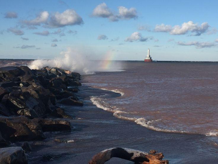 Waves crashing against a breaker wall with a lighthouse in the distance