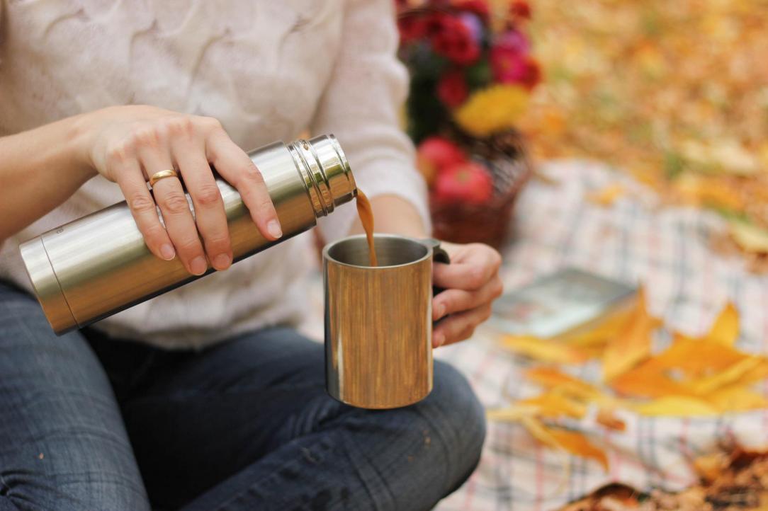 Woman sitting on a blanket on the ground, pouring tea in autumn