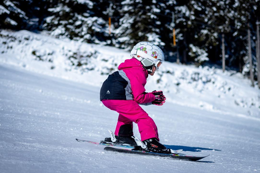 Young girl in a pink coat skiing down a hill
