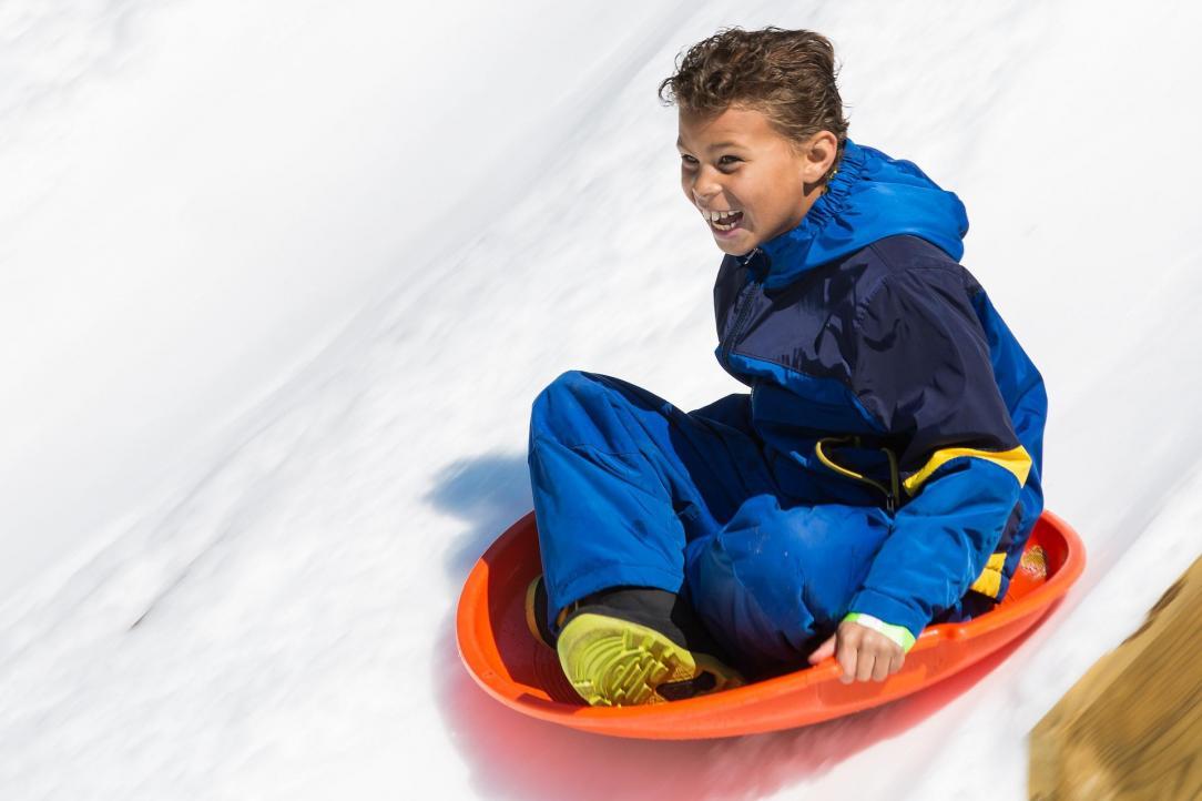 Young boy smiling sledding down a steep hill