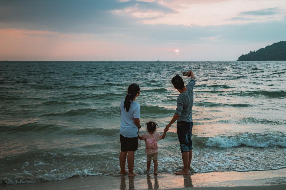 Family with young daughter taking a selfie on the beach during sunset